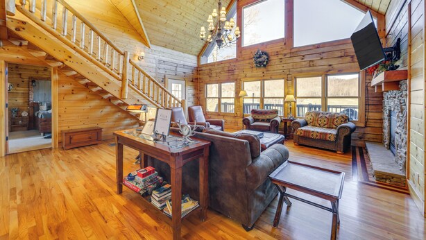 A spacious log cabin interior with a wooden staircase, leather furniture, and large windows. - Deck & Mtn Views! Luxe Log Cabin in Waynesville (Waynesville)