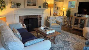 A living room with a fireplace, a sofa, a chair, a coffee table, and a television. - SUNSET BAY COTTAGE HotTub,OutdoorShower,Kayaks,Bikes,NatureTrailsToGrays,FirePit (Yarmouth Port)