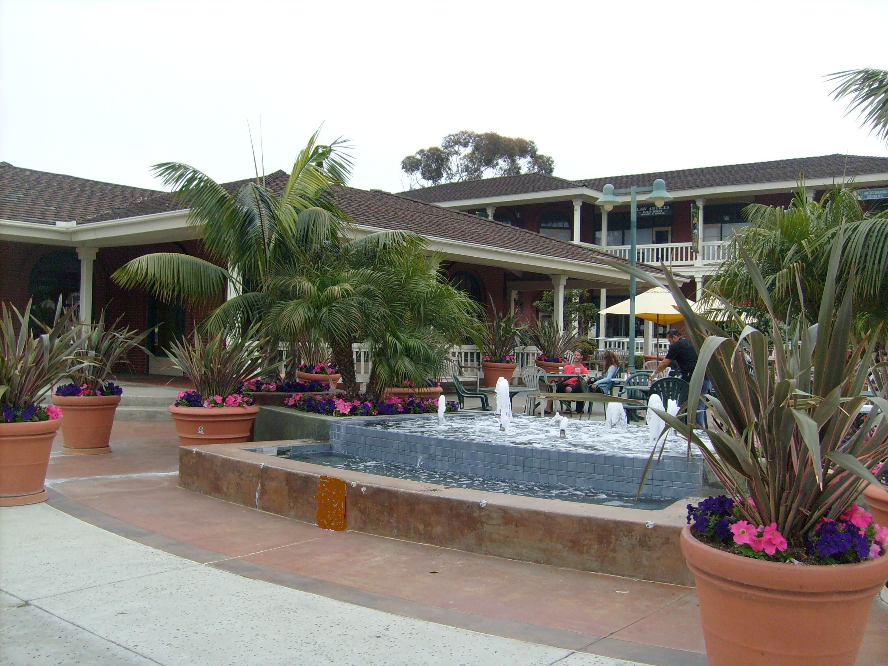 A courtyard with a fountain, potted plants, outdoor seating, and a building with a balcony.