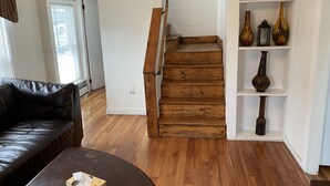 Een woonkamer met een houten trap, een zwarte leren bank en een houten salontafel.