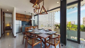 A modern dining area with a wooden table and chairs, a kitchen in the background, and a balcony with a view of buildings and greenery. - Beautiful Condo in the heart of Zona Romantica! 2BD Condo for rent in Old Town, (Puerto Vallarta)