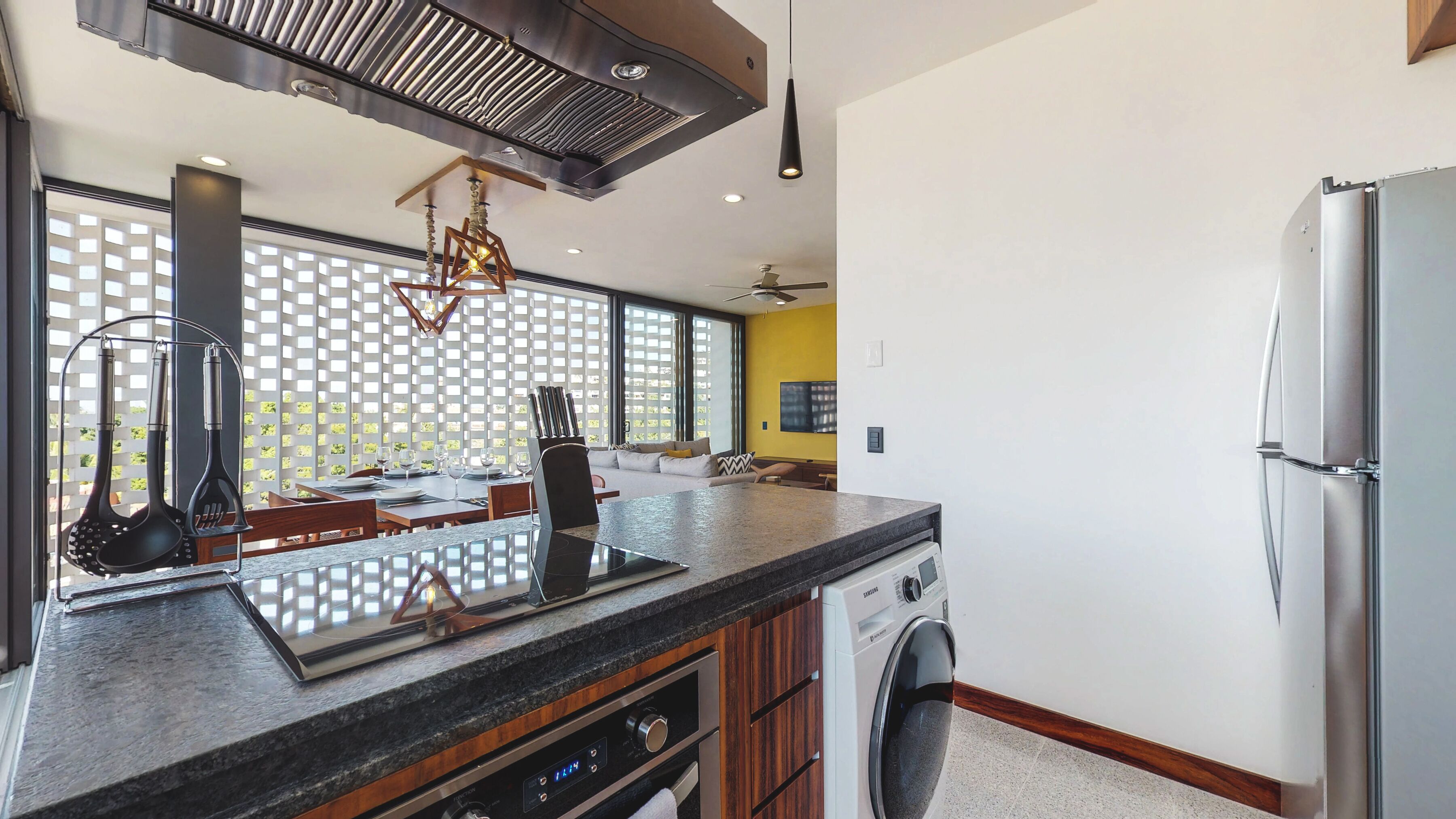 A modern kitchen with a built-in washer and dryer, a granite countertop, and a dining area with a view through a lattice window.