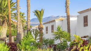 A row of white buildings with terracotta roofs, surrounded by palm trees and cacti.
