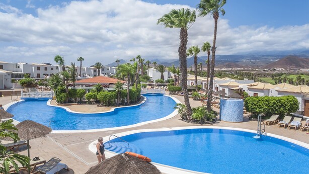 A resort with a large pool, palm trees, and a view of mountains.