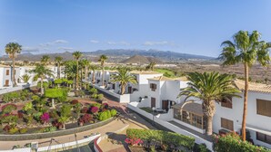 A row of white buildings with palm trees and colorful gardens.