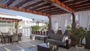 An outdoor patio with a sofa, two coffee tables, and potted plants.