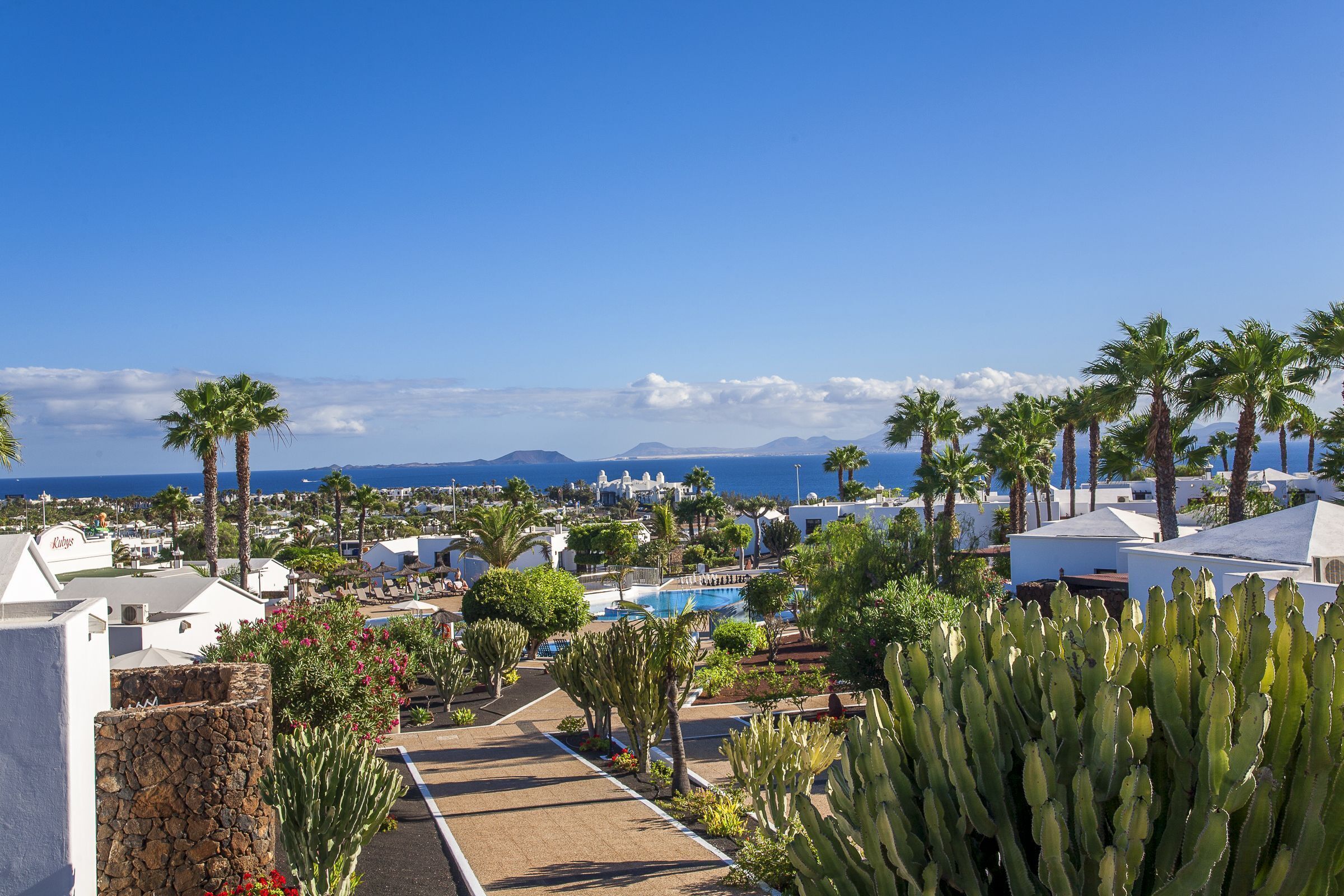 A resort with a pool, palm trees, and a view of the sea.
