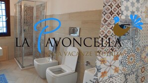 A bathroom with a glass shower enclosure, two toilets, and a decorative tiled wall. - Holiday home La Pavoncella app4 (Teulada)