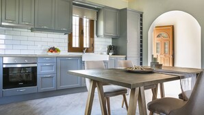 Cozinha moderna com armários cinzas, forno embutido e área de jantar com mesa e cadeiras de madeira.