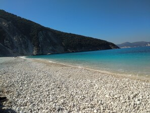 Ein Kiesstrand mit klarem türkisblauem Wasser und einer bergigen Kulisse.