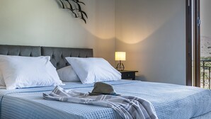 Uma cama bem arrumada com almofadas brancas e um edredom azul estampado, um objeto decorativo fixado na parede e um abajur.