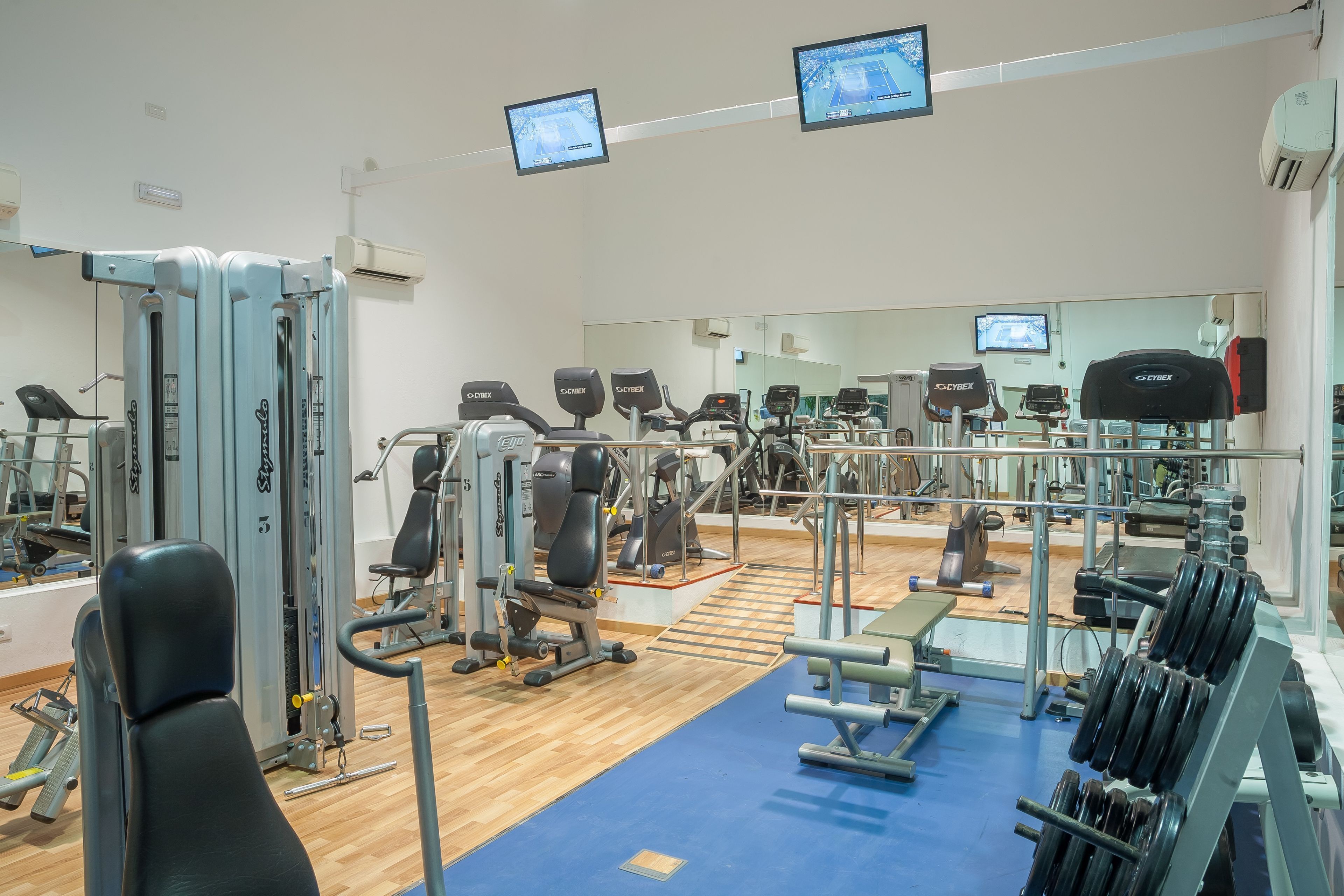 Ein Fitnessstudio mit verschiedenen Trainingsgeräten, Spiegeln und einem blauen Boden.
