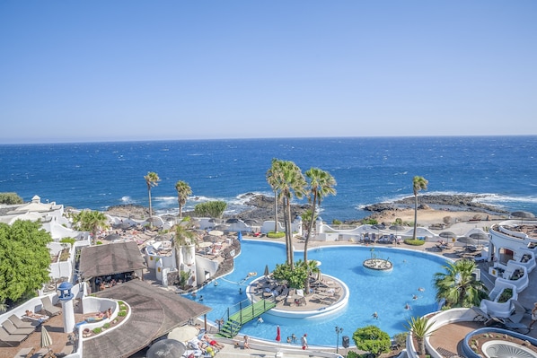 Un resort con piscina central, palmeras y vista al océano.