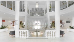 En rymlig, flervånings atrium med vita pelare, en central trappa och en stor kristallkrona.