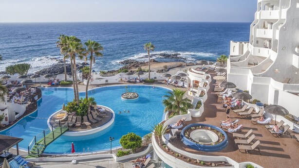 Ett semesterparadis med en stor pool, palmer och utsikt över havet.