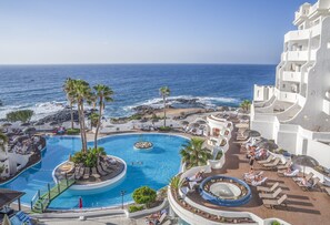 Un resort con una piscina grande, palmeras y vistas al océano.