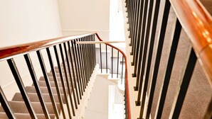A staircase with a wooden handrail and black balusters, leading to a landing with a white wall and a window.