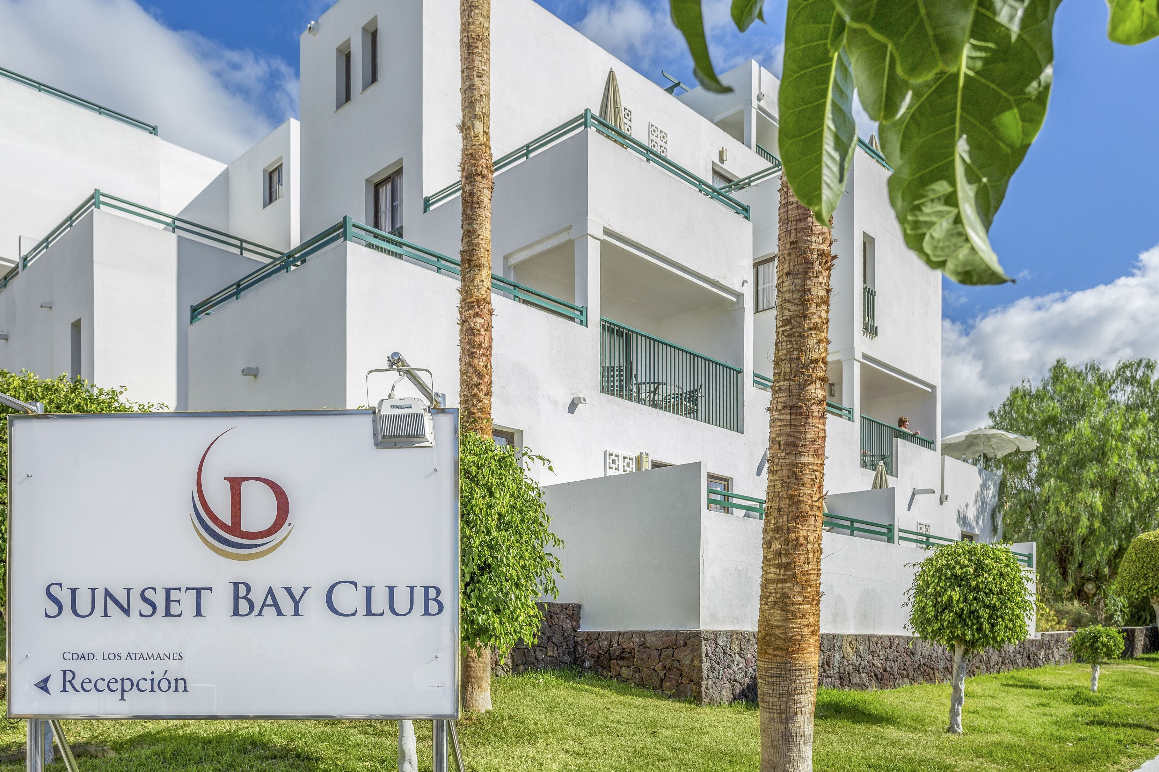A white building with balconies and a sign that reads "Sunset Bay Club."