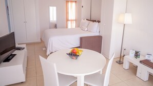 A hotel room with a bed, a TV, a desk with a computer, a table with fruit, and a lamp. - 1 Bedroom Apartment, Sunset Bay (Costa Adeje)