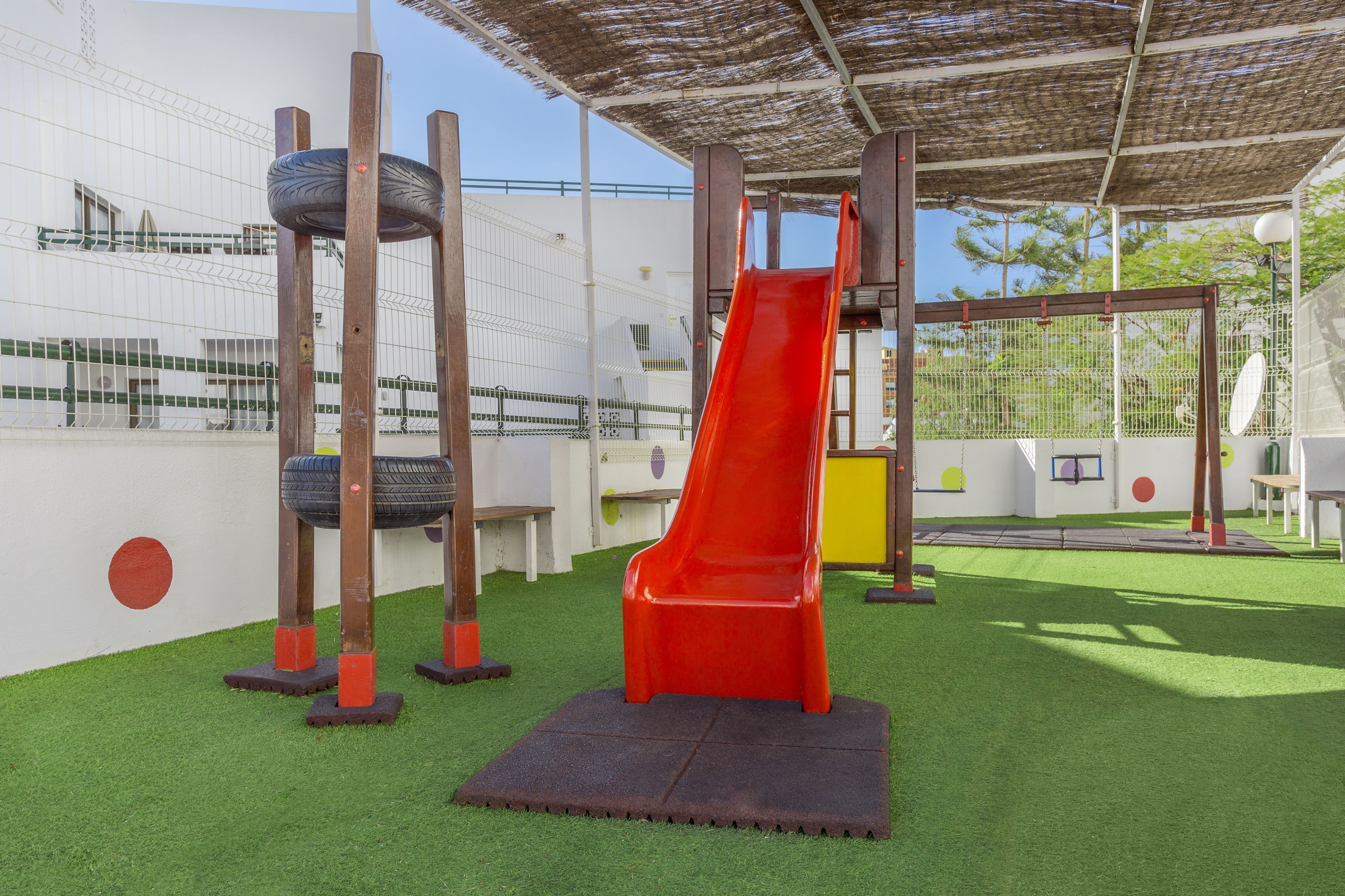 A playground with a red slide, tire swings, and a netted climbing area.