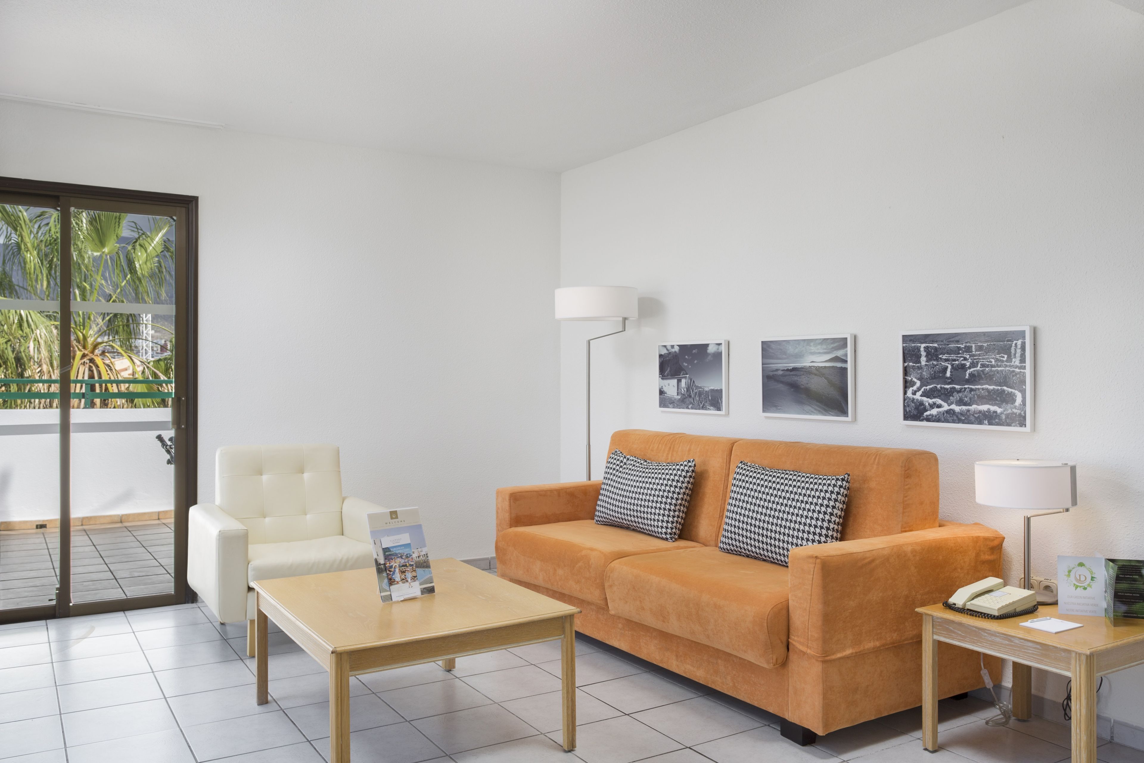 Un salon moderne avec un canapé, un fauteuil et une table basse. Des tableaux encadrés ornent le mur, et une lampe est posée sur une table d’appoint.