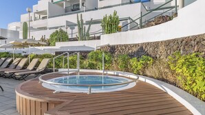 A pool area with a hot tub, lounge chairs, and a rocky landscape with cacti. - 1 Bedroom Apartment, Sunset Bay (Costa Adeje)