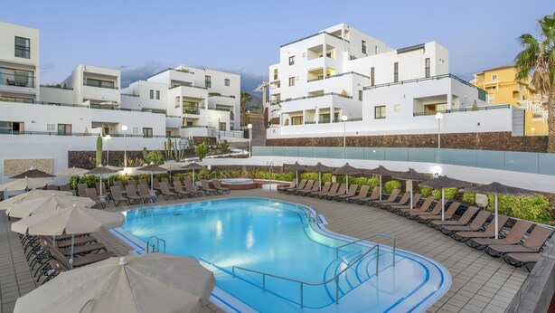 A swimming pool with sun loungers and umbrellas, surrounded by modern buildings. - 1 Bedroom Apartment, Sunset Bay (Costa Adeje)