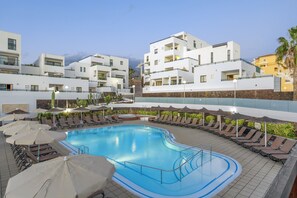 A swimming pool with sun loungers and umbrellas, surrounded by modern buildings. - 1 Bedroom Apartment, Sunset Bay (Costa Adeje)