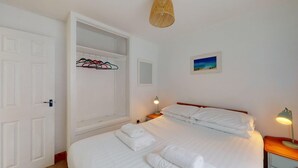 Ein Hotelzimmer mit Bett, Schrank, Nachttisch mit Lampe und einem Bild an der Wand.