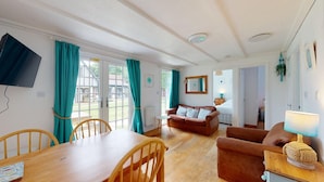 Ein gemütliches Zimmer mit einem Holztisch, zwei Sofas, einem Fernseher und Blick nach draußen.