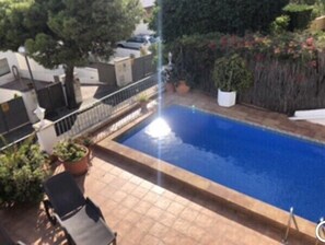 Una piscina rectangular con un borde de baldosas, rodeada de plantas en macetas y una cerca de metal.