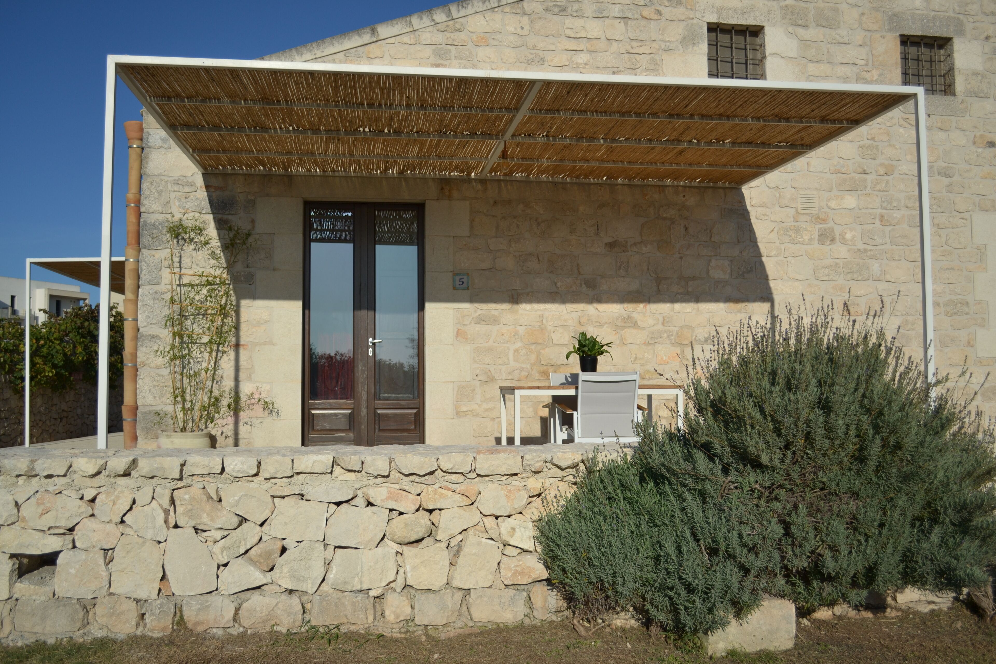 A stone building with a wooden door, a small table with a chair, and a potted plant.
