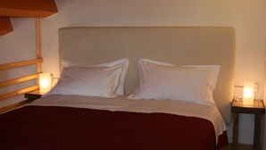Una cama con cabecera de madera, dos almohadas y una colcha roja. Hay lámparas de noche a ambos lados de la cama.