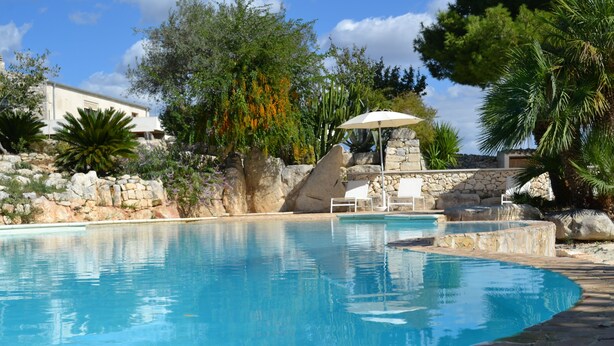 Una piscina con pared de piedra, sillas de descanso y una pérgola.