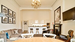 Un salón amplio con una mesa de comedor de madera, sillas blancas, un sofá y una araña.