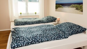 A bedroom with two beds, a window with curtains, a small plant, and a beach view painting.