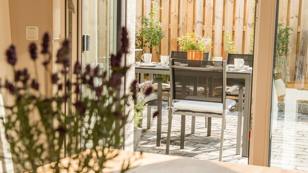A patio area with a table and chairs, a potted plant, and a wooden fence in the background.
