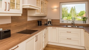 A modern kitchen with white cabinetry, a wooden countertop, a built-in oven, and a window with a view of greenery outside.