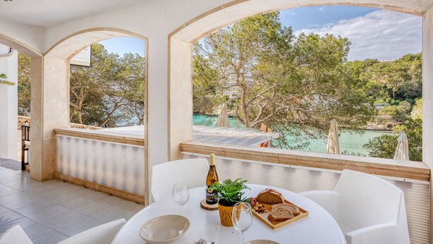 A dining area with a table set for two, a bottle of wine, and a view of a natural landscape.