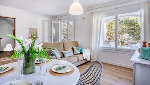 A modern living room with a sofa, dining table, and large windows.