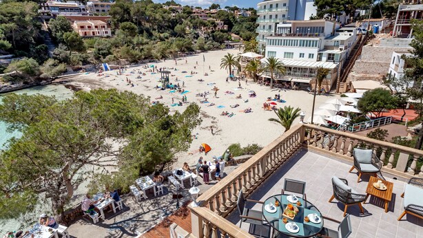 Hotel a peu de platja amb terrassa exterior, piscina i vista al mar.