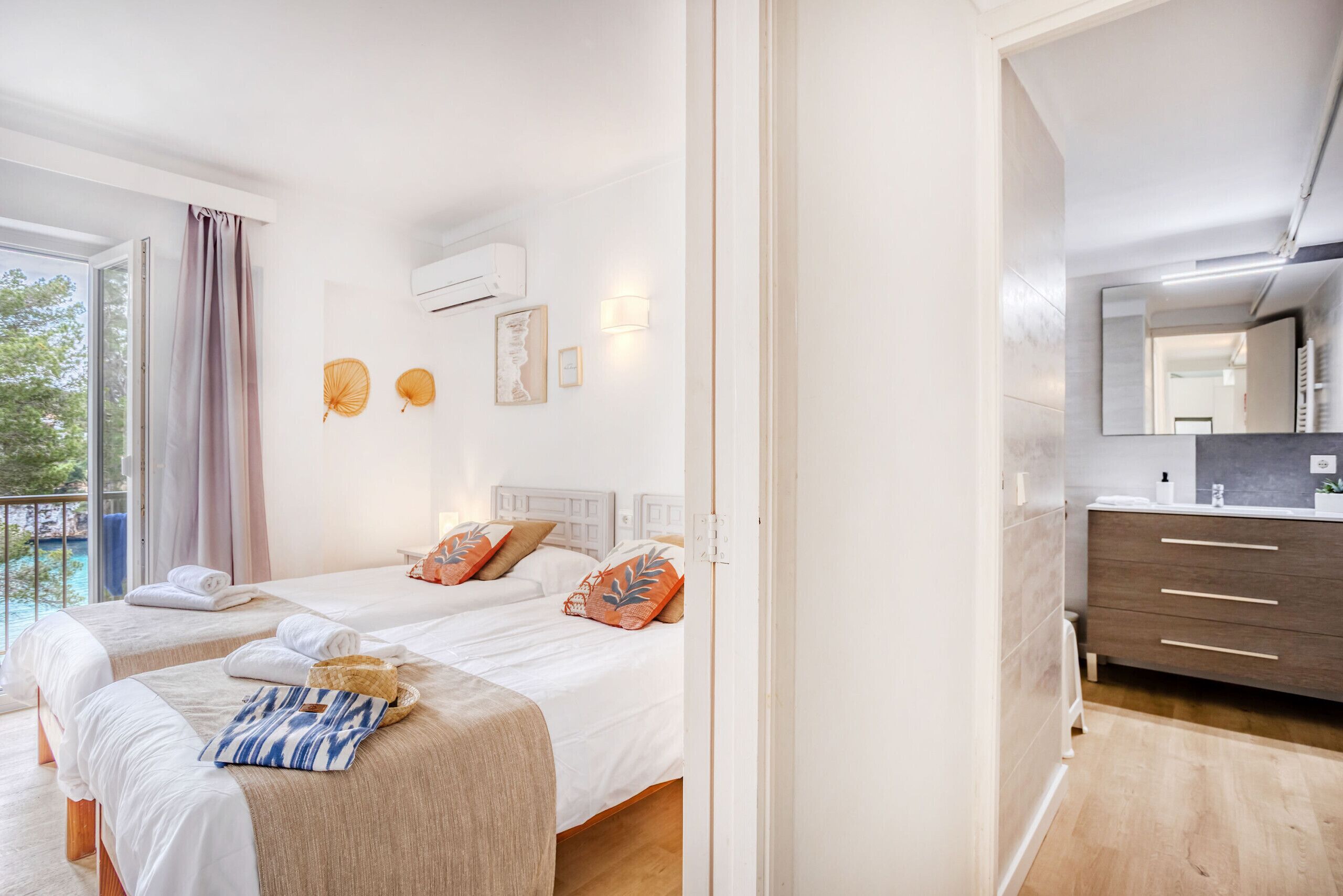 Een hotelkamer met twee bedden, een balkon, een badkamer met spiegel en een houten vloer.