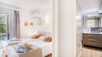 Een hotelkamer met twee bedden, een balkon, een badkamer met spiegel en een houten vloer.