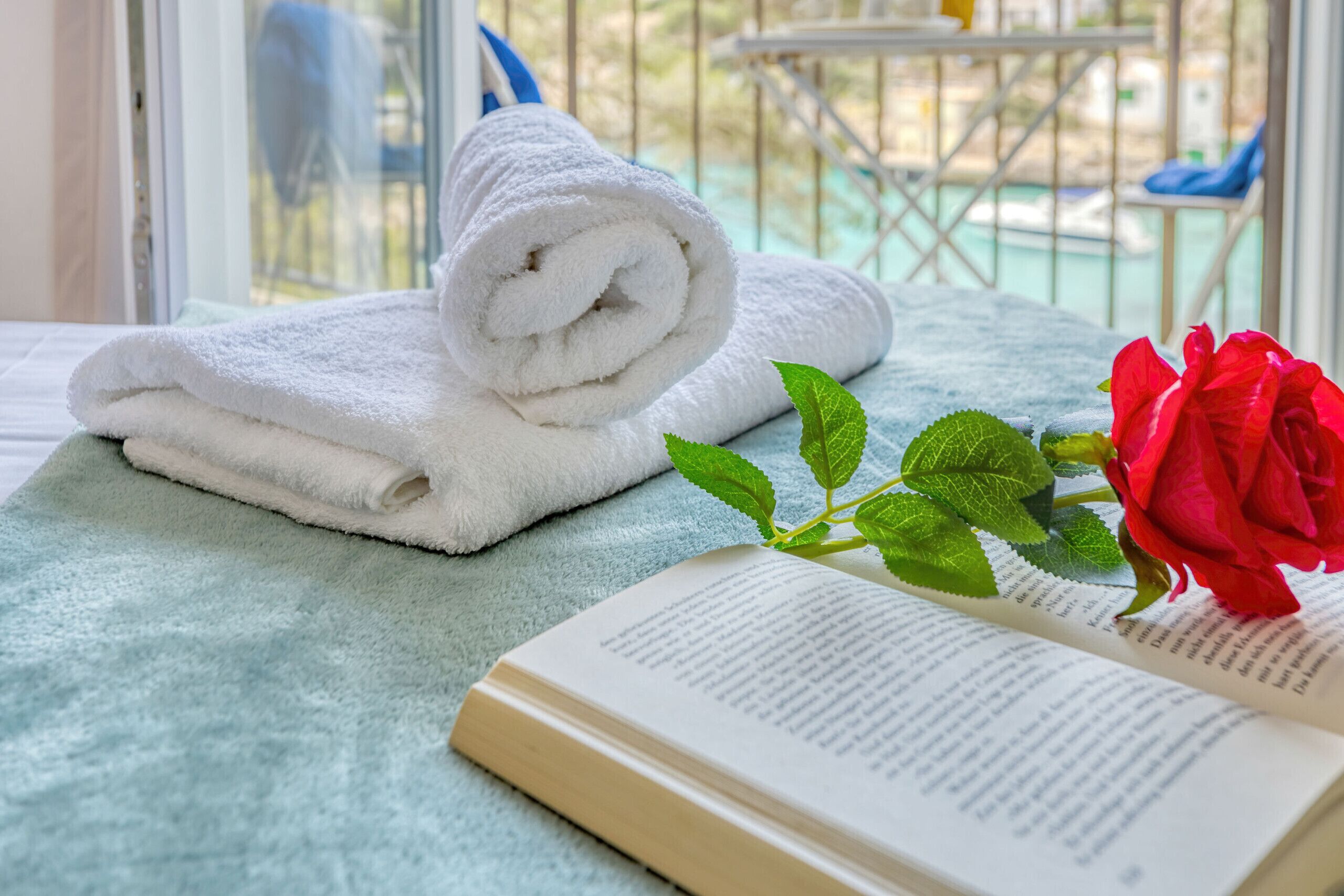 Une serviette blanche soigneusement pliée, une rose rouge et un livre ouvert sur une surface bleu clair.