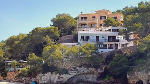 Un edificio de varios pisos con balcones, ubicado en una ladera con vista a un mar azul y despejado.