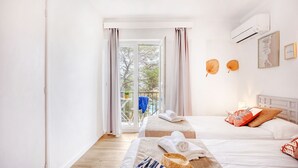 Un dormitorio luminoso con dos camas, un balcón y un equipo de aire acondicionado.