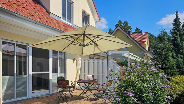 A patio with a table and chairs, a large umbrella, and a white fence.