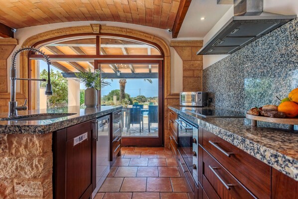 A kitchen with granite countertops, wooden cabinets, and a view through an archway to an outdoor patio.