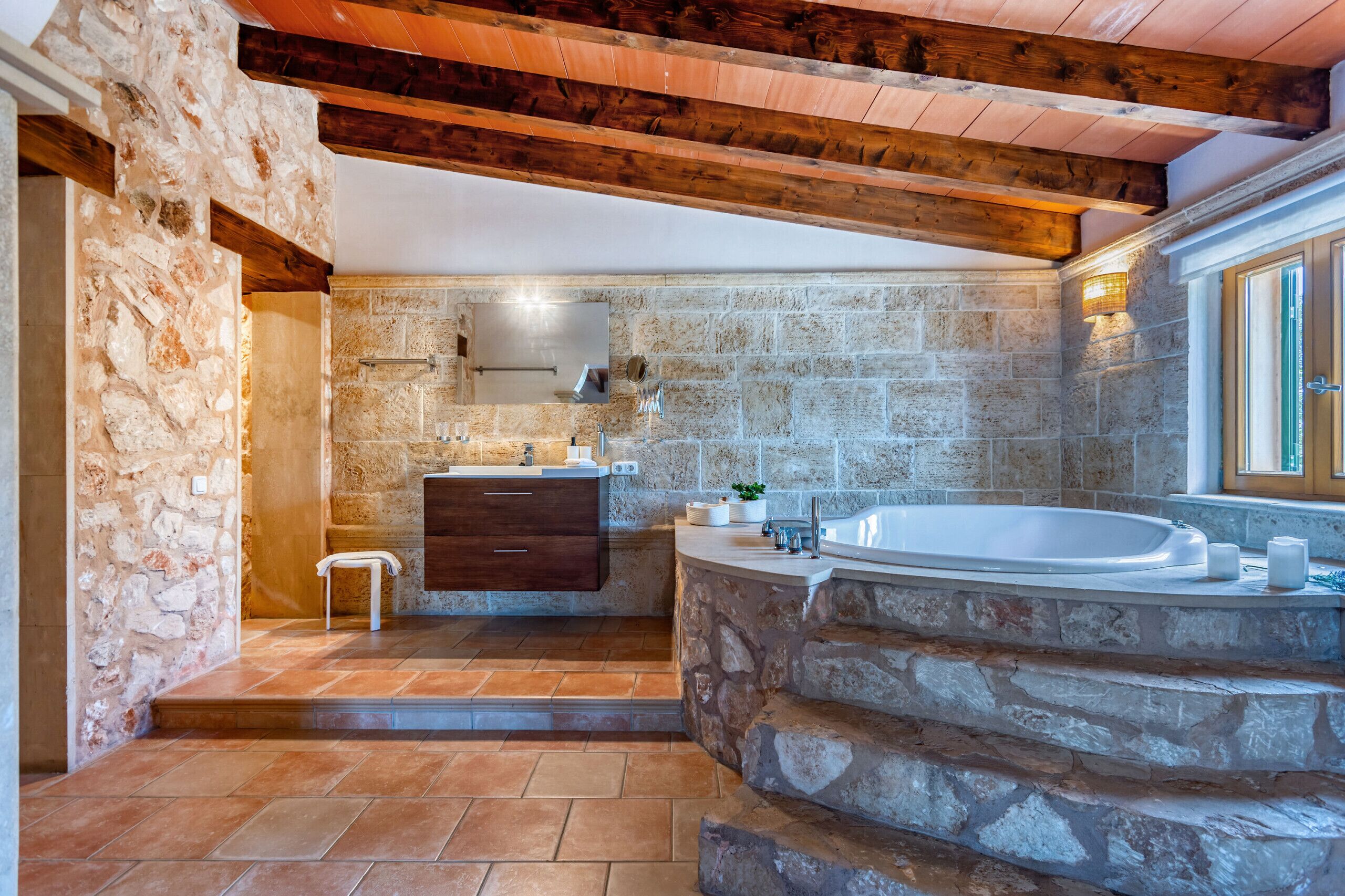 A bathroom with stone walls, a wooden ceiling, a bathtub, and a vanity with a mirror.