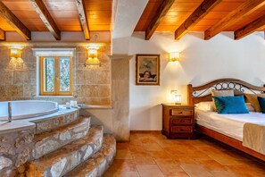 A bedroom with a stone staircase leading to a bathtub, a wooden headboard, and a nightstand with a lamp.